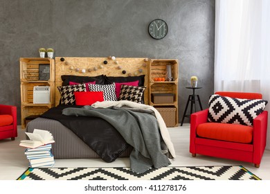 Grey interior with red armchairs, big bed, pattern carpet and pillow