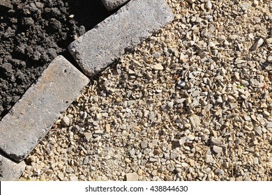 Grey Landscape Cobblestone Pavers Are Edging A Garden With Black Dirt Top Soil, Separating It From A Gravel Path