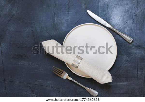 grey napkin in a silver ring,
white craft plate, cutlery on dark stone table. Top view, copy
space, Table setting. background for menu, layout, place for
text