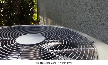 Grey Outdoor AC Condenser Unit Next To Bush And Stucco Wall