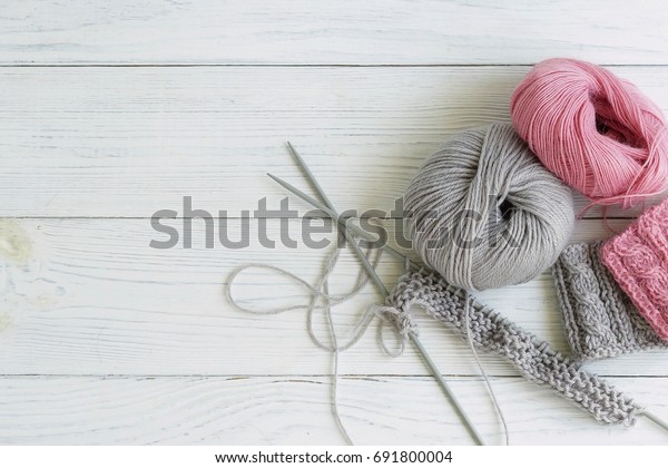 Grey and pink  knitting\
wool and knitting needles on white wooden background. top view.copy\
space