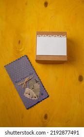 Grey postcard with two hearts from note paper, box on bright yellow background. Valentines day present. Top view, copy space, vertical