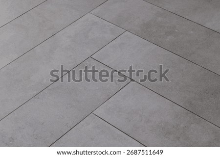 Grey rectangular tile texture in herringbone pattern imitating natural stone or concrete, decorative ceramic surface
