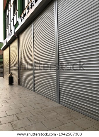 Grey roller shutters of a small storewith some sun lights on it in a town.