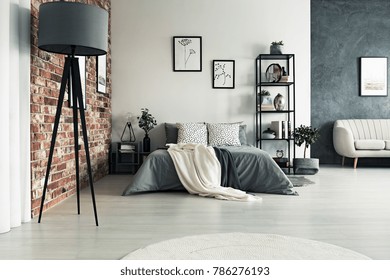 Grey roomy apartment with king size bed, sofa, lamp and one decorative brick wall