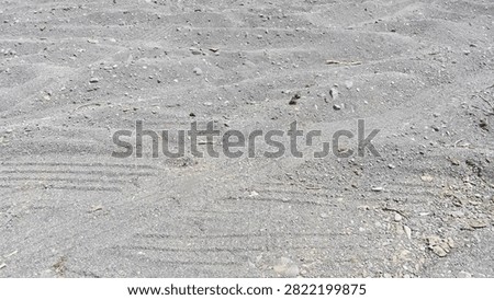 Grey sand surface background with uneven natural waves, small pebbles and dry gravel texture on a beach shore in bright daylight outdoor setting