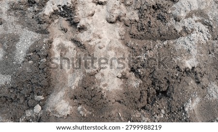 Grey sand. The surface is uneven and bumpy, featuring wet, dark clumps scattered across areas of dry, finer light grey sand. The contrasting tones and rough composition create a natural, earthy texture perfect for a background.
