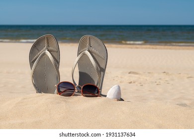 Grey sandals at the beach on a beautiful sunny day. Slippers in the sand by the sea. Flip flops at the shore by the ocean.