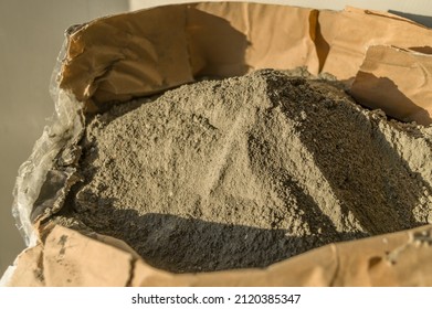 Grey sand-concrete dry mix in an open paper bag. Concrete dry powder for leveling walls and floors. Repair in the house with your own hands. DIY. Selective focus
