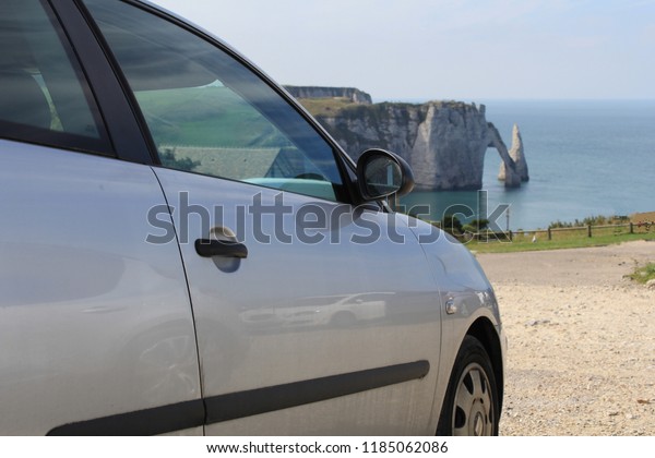 a grey seat ibiza car closeup at a parking in\
etretat, france, with the famous white cliffs of the alabaster\
coast in the background in\
summer\
