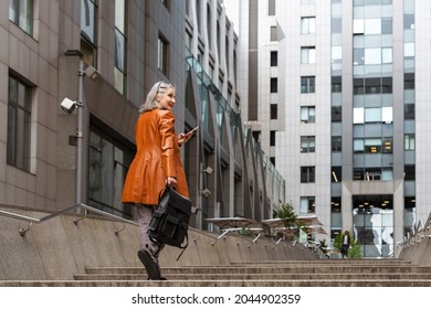 Grey senior woman using mobile phone while going up stairs outdoors
