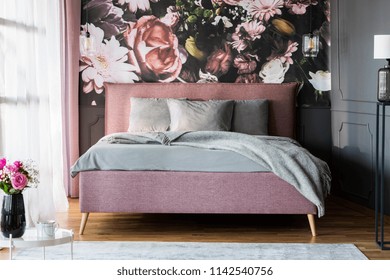 Grey sheets on pink bed in feminine bedroom interior with flowers print on the wall. Real photo