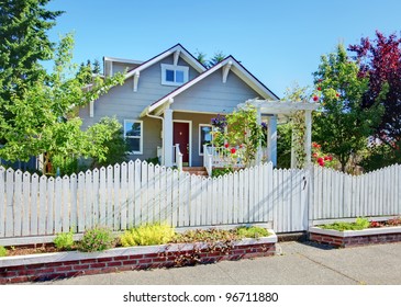 Grey small cute house with white fence and roses.
