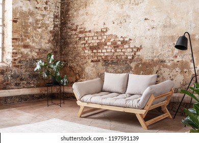 Grey Sofa Between Plant And Black Lamp In Wabi Sabi Loft Interior With Red Brick Wall. Real Photo