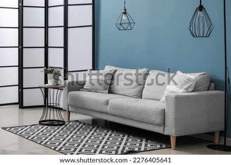 Grey sofa with cushions, lamps and houseplant on table in interior of living room