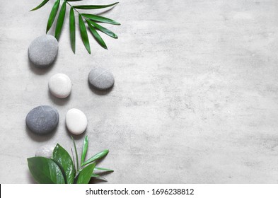 Grey spa background, spa concept, palm leaves and grey stones, top view.