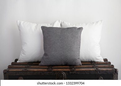 Grey Square Cushion Mockup With Two White Square Cushions On Top Of An Old Vintage Suitcase.