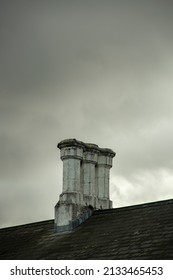 Grey Stone Chimney On Top Of A House Roof. Stormy, Cloudy Sky. Sad, Eerie Atmosphere. No Smoke Or Steam. Day Time. House Looks Old And And Abandoned. No People. Copy Space To Add Text.