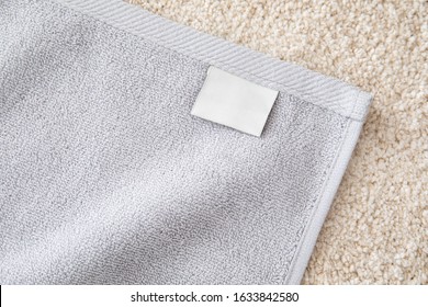 Grey Terry Towel With White Empty Label On Beige Pile Carpet.