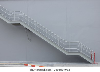 A grey wall with a metal staircase leading up to it. The staircase is made of metal and has a red and white stripe