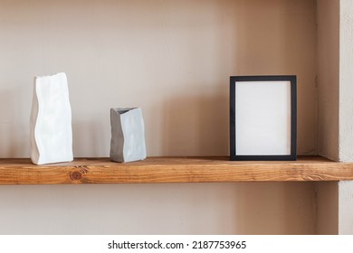 Grey And White Colored Vases, Blank Black Photoframe On Wooden Shelf Against Grey Wall. Home Decor.