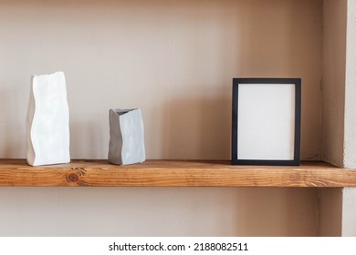 Grey And White Colored Vases, Blank Black Photoframe On Wooden Shelf Against Grey Wall. Home Decor.