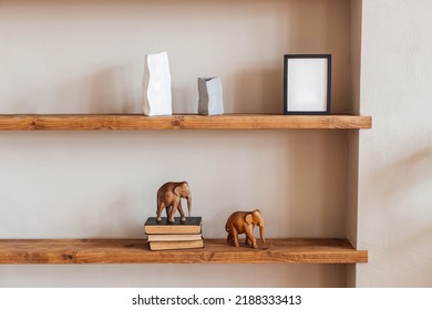 Grey And White Colored Vases, Wooden Figures Of Elephants, Blank Black Photoframe And Stack Of Books On Wooden Shelf Against  Grey Wall. Home Decor.