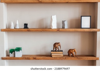 Grey And White Colored Vases, Wooden Figures Of Elephants, Blank Black Photoframe And Stack Of Books On Wooden Shelf Against  Grey Wall. Home Decor.