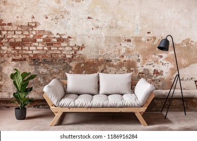 Grey Wooden Sofa Between Plant And Black Lamp In Living Room Interior With Red Brick Wall. Real Photo