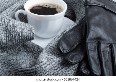 Grey wool scarf and leather gloves are surrounded by a hot cup of coffee with shallow depth of focus