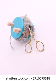 Grey Yarn Wrapped Around A Pompom Maker With A Golden Scissors Cutting It, Isolated On White Background