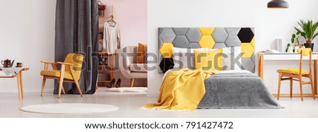 Grey and yellow bedding on bed with bedhead in bright bedroom interior with wardrobe and yellow vintage armchair