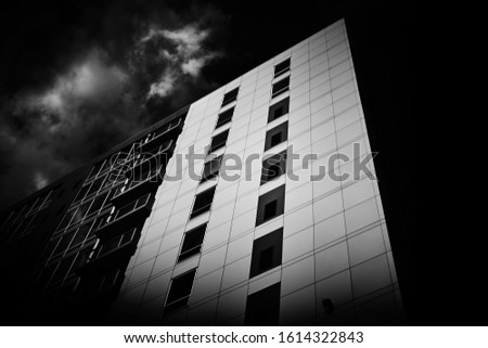A greyscale low angle shot of an apartment building under the storm clouds