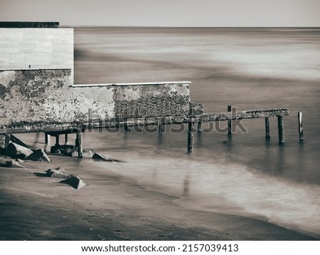 A greyscale shot of an abandoned old structure on the sea