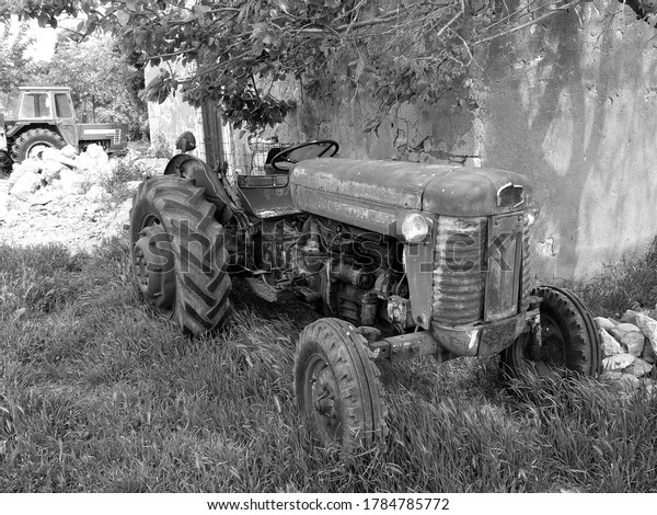 A\
greyscale shot of an old tractor in a rural\
area