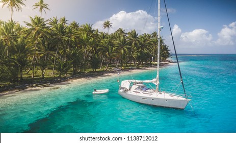 A grey-white sailing yacht anchoring in crystal clear turquoise water in front of the paradisiacal San Blas Islands in Panama with green palm trees in the background. (Stylized version)