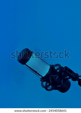 Grid. Hex. A lone microphone stands against a vibrant blue wall, illuminated by a captivating azure glow.