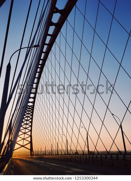 Grid of ropes of modern suspension bridge, viewed\
from low angle against beautiful morning sky with colors gradient.\
Novosibirsk, Russia