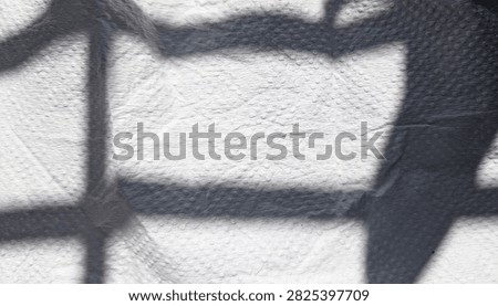 Grid shadows casting on dimpled white fiber material surface.