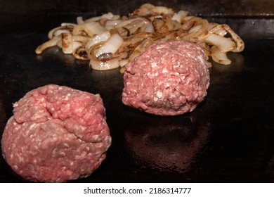 Griddle Cooking.  Ground Beef Balls On Griddle Ready To Make Smash Burgers.  Onions Cooking In Background.