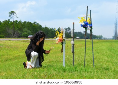 A grieving bereaved woman kneeling down to placing flowers on crosses beside a busy road marking the location of where her friend was killed in a terrible drunk driver car wreck.