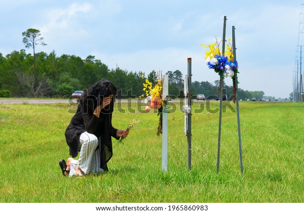 A grieving\
bereaved woman kneeling down to placing flowers on crosses beside a\
busy road marking the location of where her friend was killed in a\
terrible drunk driver car\
wreck.