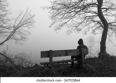 Grieving Man Sitting Alone On A Bench At A Lake On A Foggy Day.