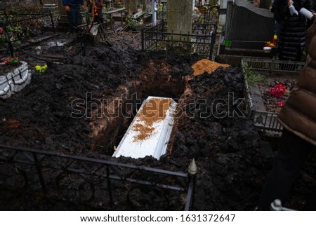 Grieving relatives bury a white coffin in a pit, throwing the coffin to the ground