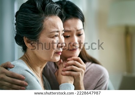 grieving senior asian mother and adult daughter holding hands