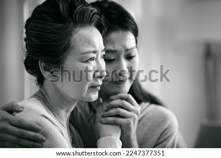 grieving senior asian mother and adult daughter holding hands, black and white
