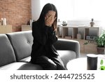 Grieving young Asian woman crying on sofa at funeral