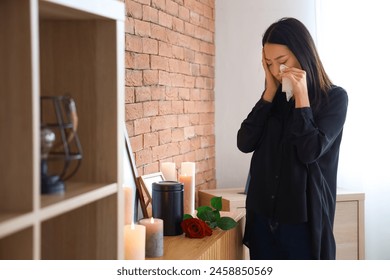 Grieving young Asian woman with mortuary urn crying at funeral