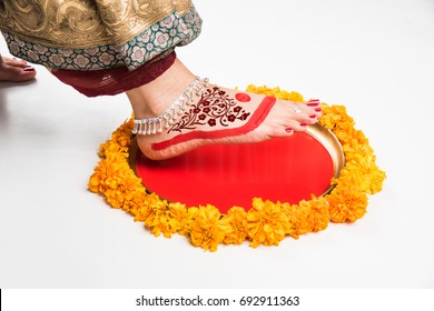 Griha Pravesh Concept - Rright feet of a Newly married Indian Hindu bride in Saree stepping in a plate filled with liquid kumkum tbefore entering house for the first time
