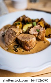 Griled Pork Tenderloin With Roast Potatoes And Pepper Sauce On White Plate On Wood Table